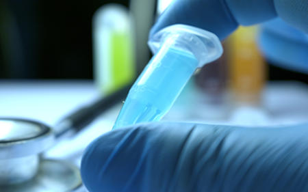 A laboratory technician holding a tube containing liquid for use in medical research.